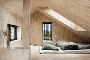 Ein Schlafzimmer mit schrägverdeckter Decke, einem Bett und einem Fenster mit Blick auf Grünfläche.