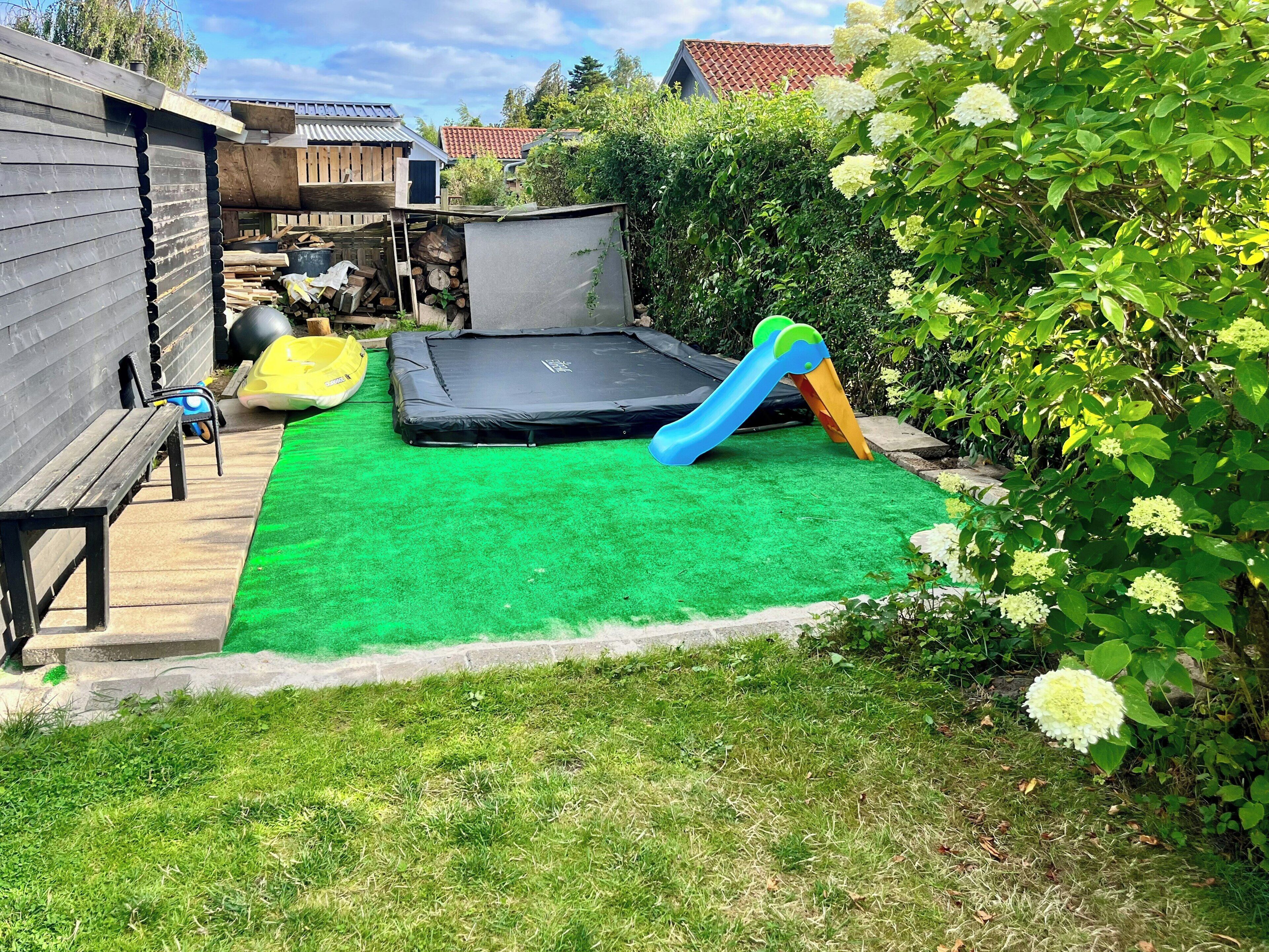 A backyard with a trampoline, a slide, and a wooden bench.