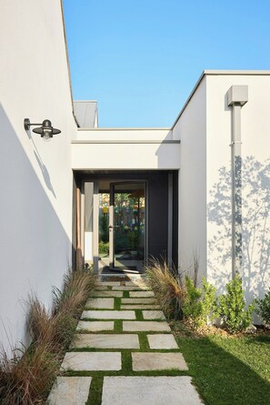 A modern house with a stone pathway leading to a glass door, surrounded by greenery. - New villa with pool in Sainte-Marine (Combrit)
