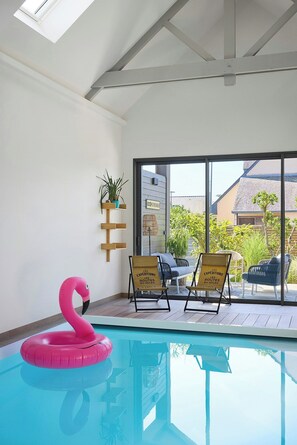 A swimming pool with a pink flamingo float, two lounge chairs, and a glass door leading outside. - New villa with pool in Sainte-Marine (Combrit)