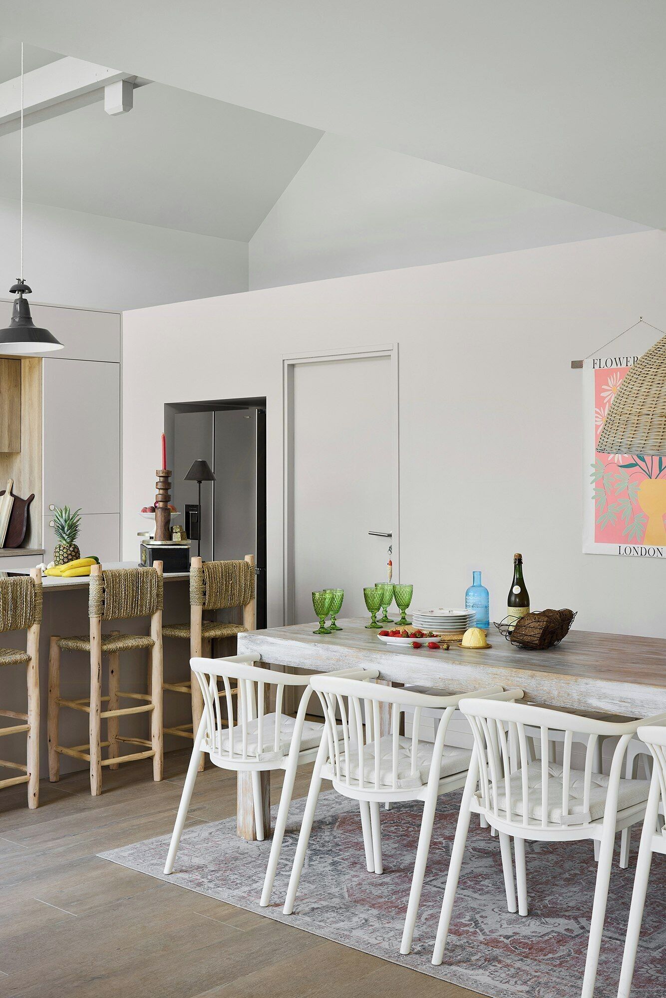 A modern dining area with a white table and chairs, a kitchen area with a refrigerator, and a hanging light fixture.