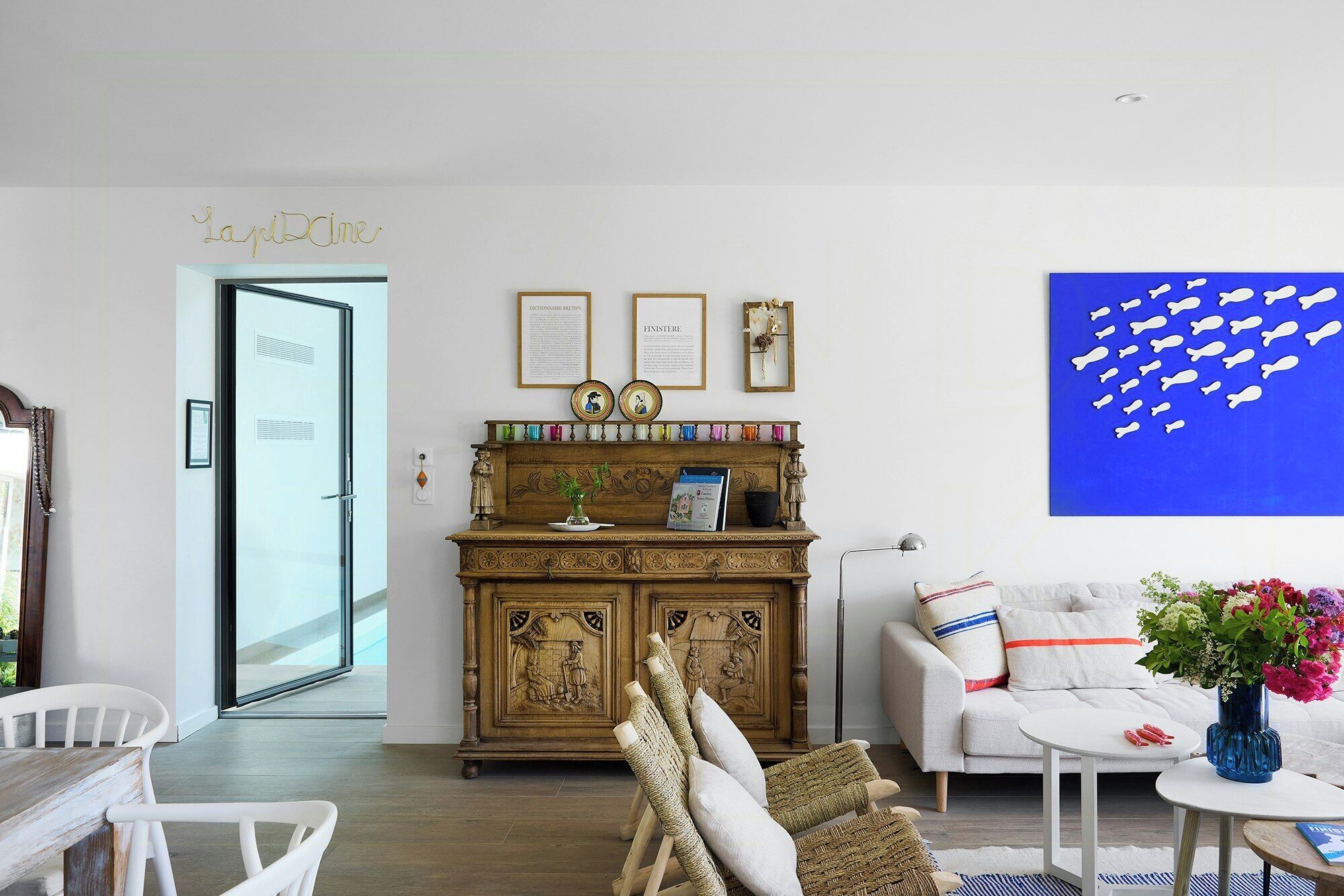 Una sala de estar con un aparador de madera, un sofá blanco, un cuadro azul y una puerta con la etiqueta 'La Piccole'.