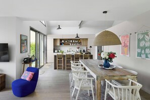 A modern kitchen with wooden cabinets, a dining area with a wooden table and white chairs, and a blue bean bag chair. - New villa with pool in Sainte-Marine (Combrit)