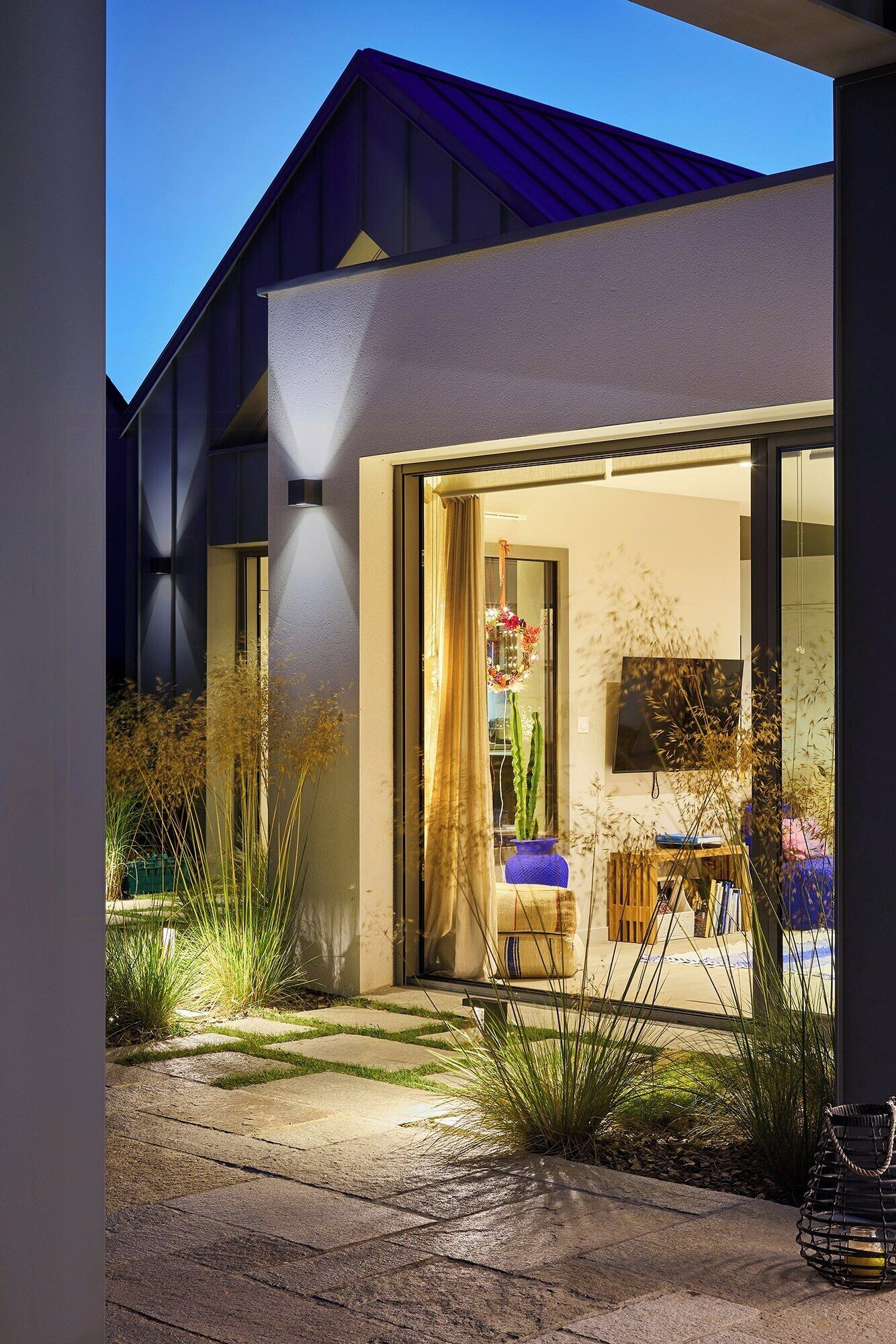 Une maison moderne dotée d’une grande porte vitrée, d’un toit plat et d’un jardin agrémenté de plantes et d’un banc.
