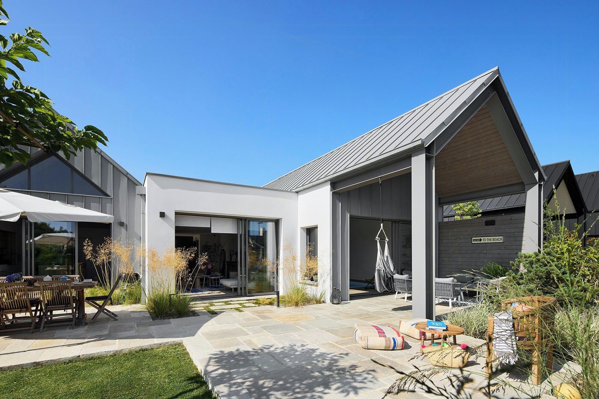 A modern house with a covered patio, outdoor seating, and a clear path leading to the entrance.