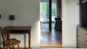 A room with a wooden desk, a chair, a lamp, a television, and a view of a balcony with a table and chairs. - Apartment in renovated stable near UNESCO cliffs (Præstø)