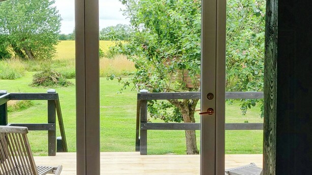 A room with a white table, two candles, a patterned rug, and a view of a deck with chairs and greenery outside. - Apartment in renovated stable near UNESCO cliffs (Præstø)