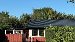 Un edificio rosso con tetto nero, immerso in un prato curato e delimitato da un siepe.