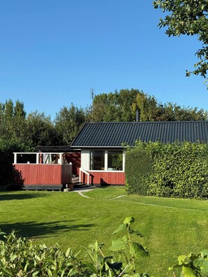 A red building with a black roof, surrounded by a well-maintained lawn and a hedge. - Holiday home in peaceful surroundings (Dannemare)