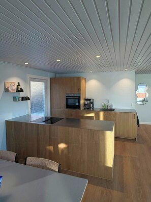 A modern kitchen with wooden cabinetry, a built-in oven, and a microwave. - Holiday home in peaceful surroundings (Dannemare)