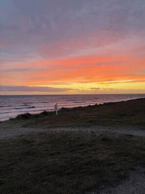 A coastal landscape with a grassy foreground and a sunset over the ocean. - Holiday home in peaceful surroundings (Dannemare)