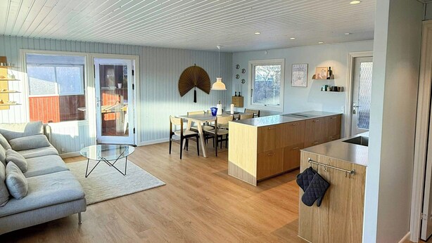 Un soggiorno moderno con divano, zona pranzo, isola della cucina e pavimento in legno.