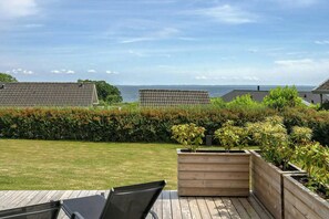 Eine Terrasse mit Meerblick, Holz-Pflanzkästen mit Sträuchern und einer Hecke.