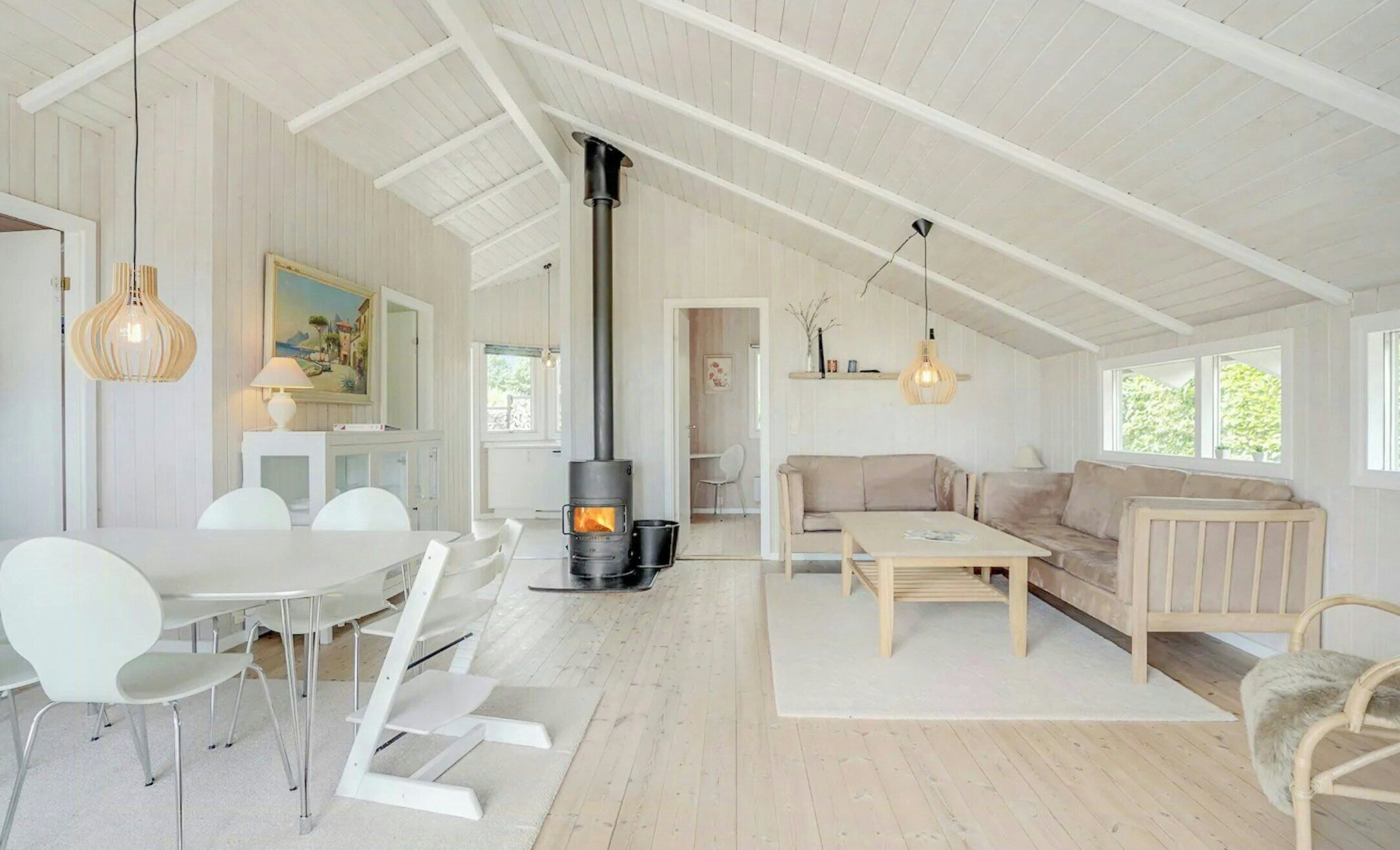 A spacious loft with a high ceiling, a central wood-burning stove, white furniture, and large windows.