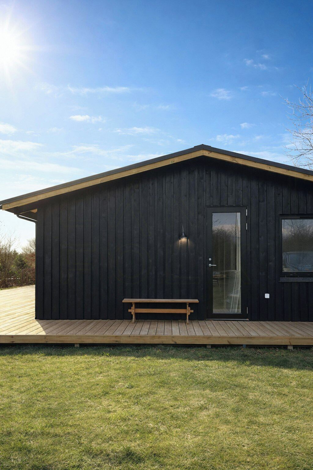 Un bâtiment en bois noir, avec un banc devant, une porte et une fenêtre.