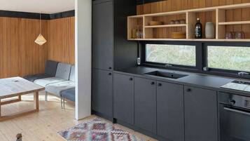 A modern kitchen with dark cabinets, a built-in sink, and a window overlooking a garden.