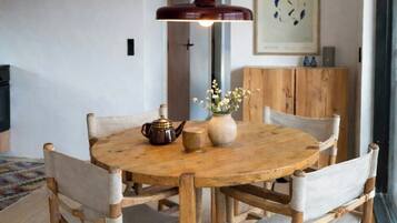 Un coin repas comprenant une table ronde en bois, quatre chaises, un luminaire suspendu et un meuble en bois.