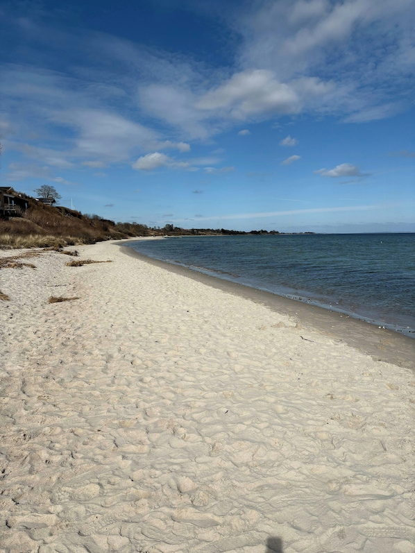 Ein sandiger Strand mit blauem Himmel und ruhigem Wasser.