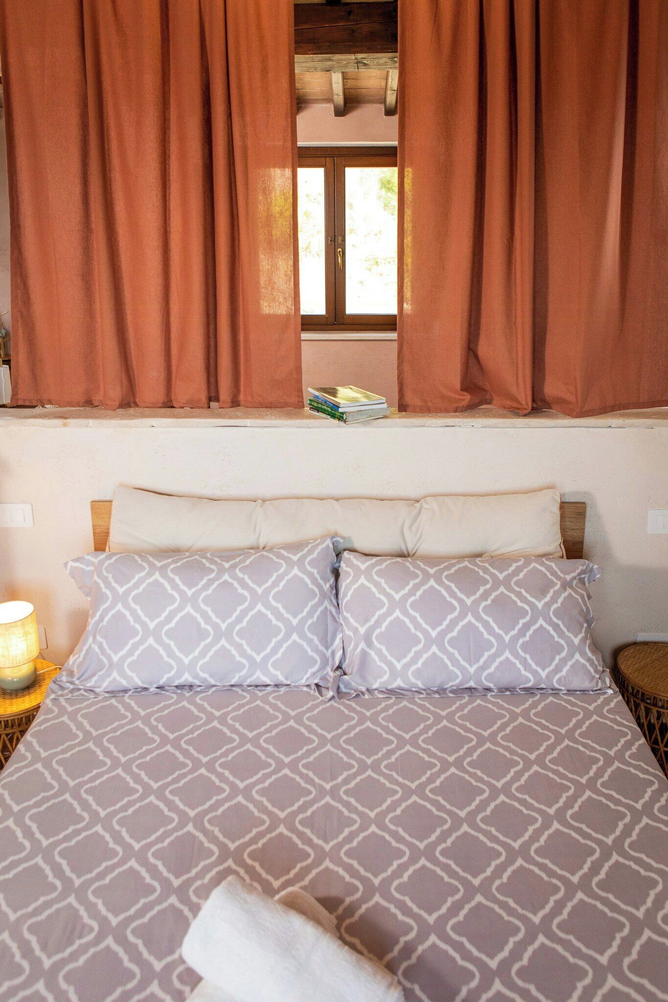 A bed with patterned bedding, a bedside lamp, and brown curtains.