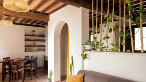 A dining area with a wooden table and chairs, a sofa with a cushion, and a window with bamboo plants. - Panoramic refuge on Monte Pelato (Gualdo Cattaneo)