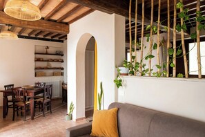Ein Essbereich mit Holztisch und Stühlen, einer Couch mit Kissen und einem Fenster mit Bambuspflanzen.
