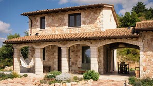 A stone building with a tiled roof, a hammock, and a patio with a table and chairs. - Panoramic refuge on Monte Pelato (Gualdo Cattaneo)