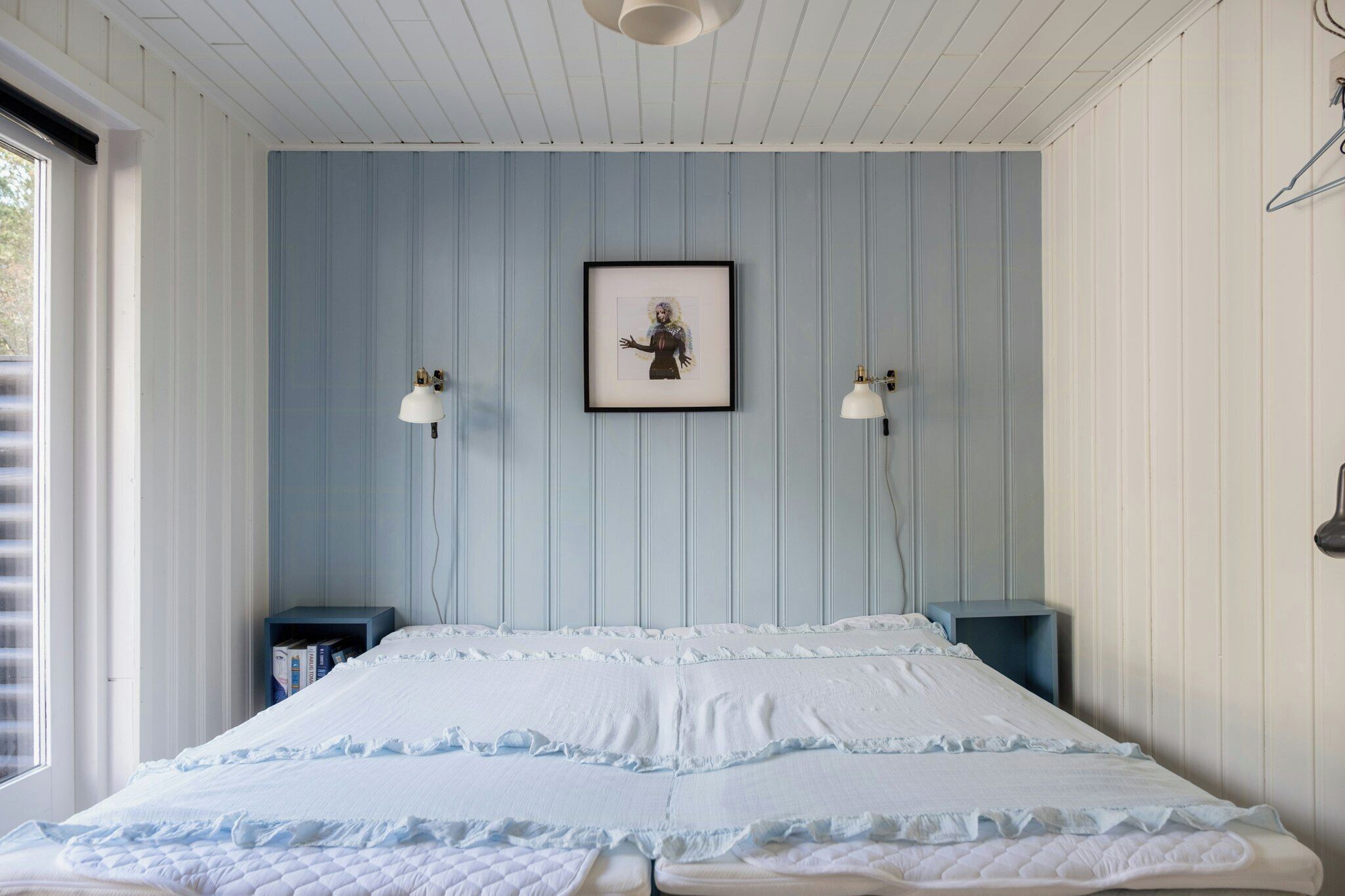 Een slaapkamer met een bed, twee nachtkastjes, een lijst met een afbeelding aan de muur en een raam.