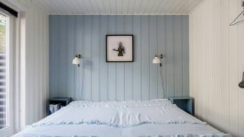 Een slaapkamer met een bed, twee nachtkastjes, een lijst met een afbeelding aan de muur en een raam.