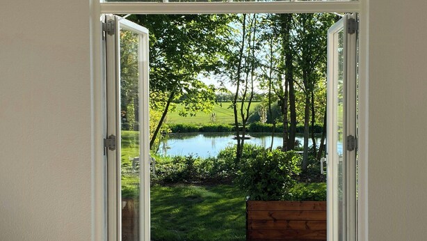 An open door leading to a garden with a pond and trees. - Historic cottage by the lake in South Jutland (Branderup J)