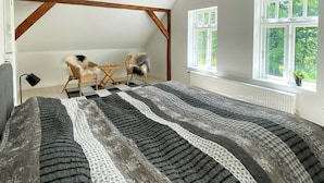 A bedroom with a large bed, two chairs, a window, and exposed wooden beams. - Historic cottage by the lake in South Jutland (Branderup J)