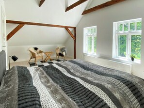 Ein Schlafzimmer mit einem großen Bett, zwei Stühlen, einem Fenster und freiliegenden Holzbalken.
