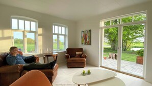 A modern living room with a large window, a brown leather sofa, a white coffee table, and a brown armchair. - Historic cottage by the lake in South Jutland (Branderup J)