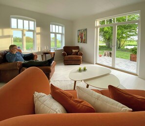 Ein modernes Wohnzimmer mit großem Fenster, einem braunen Ledersofa, einem weißen Couchtisch und einem braunen Sessel.
