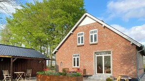 A brick house with a large window, a wooden deck, and a garden with chairs. - Historic cottage by the lake in South Jutland (Branderup J)