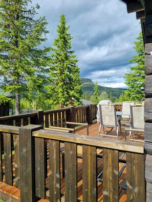 Eine Holzterrasse mit Sitzgelegenheiten im Freien, umgeben von Bäumen und einem Bergpanorama.