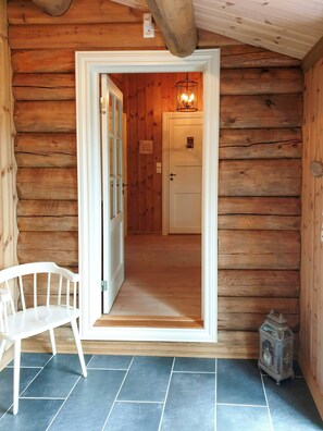 Ein Holzhütten-Interieur mit einer Tür, die zu einem Raum führt, einem weißen Stuhl und einem Laternen auf dem Boden.