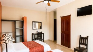 Quarto de hotel com duas camas, uma escrivaninha, uma cadeira, um guarda-roupa, uma televisão e um ventilador de teto.