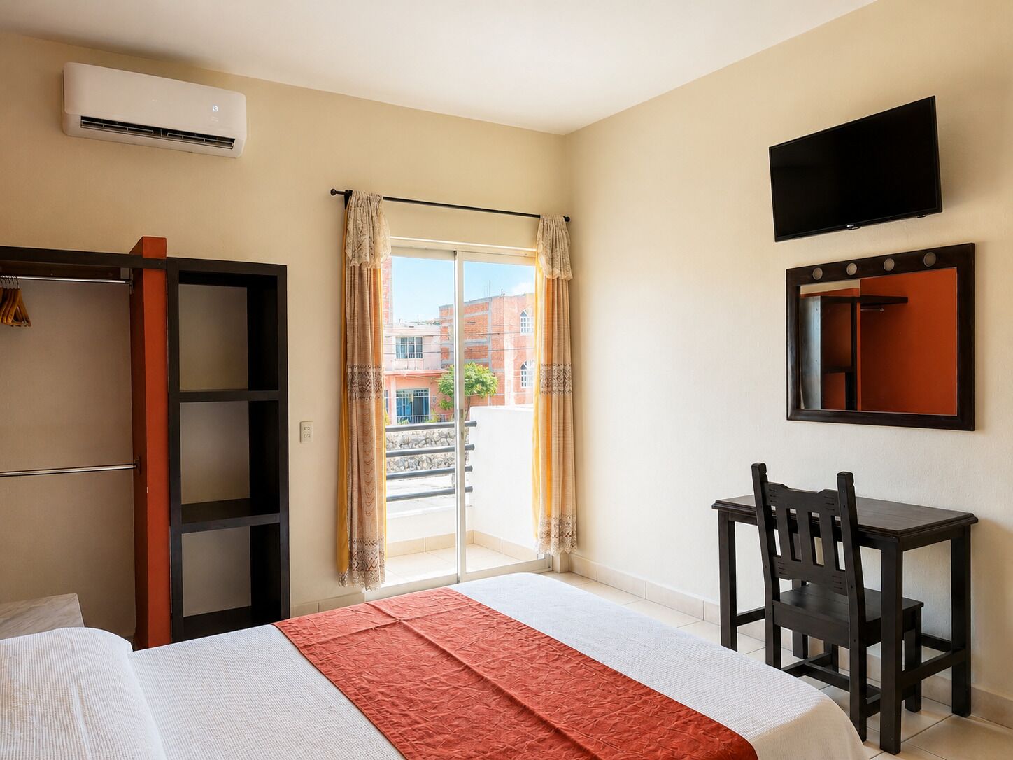 A hotel room with a bed, a desk, a chair, a television, and an air conditioning unit.