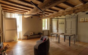 A room with exposed wooden beams, a dining table, chairs, a sofa, and a window with a view. - Farmhouse among hazelnut groves in the Langhe (Cherasco)