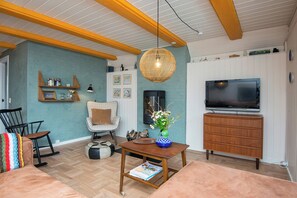 A living room with a wooden table, a sofa, a television, and a decorative hanging light. - 1960s family home near St Sjørup Beach (Ørsted)