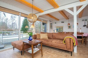 A spacious living area with a brown leather sofa, a wooden coffee table, and a wicker pendant light. - 1960s family home near St Sjørup Beach (Ørsted)