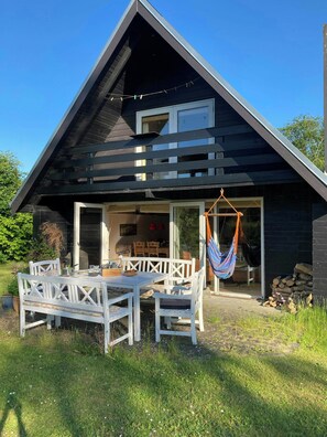 A modern house with a dark exterior, a dining area with white furniture, and a hammock. - 1960s family home near St Sjørup Beach (Ørsted)