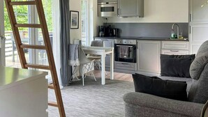 A modern loft apartment with a kitchen, dining area, and a loft bedroom with a large window. - Mini house with sandy beach and sauna (Olofstorp)