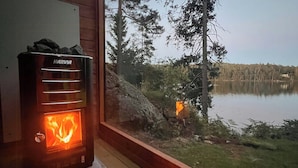 A Harvia wood-burning stove in a cabin with a view of a lake and forest. - Mini house with sandy beach and sauna (Olofstorp)