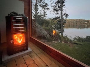 Ein Harvia Holzofen in einer Hütte mit Blick auf See und Wald.