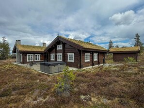 A wooden cabin with a thatched roof, a covered outdoor seating area, and a stone chimney.