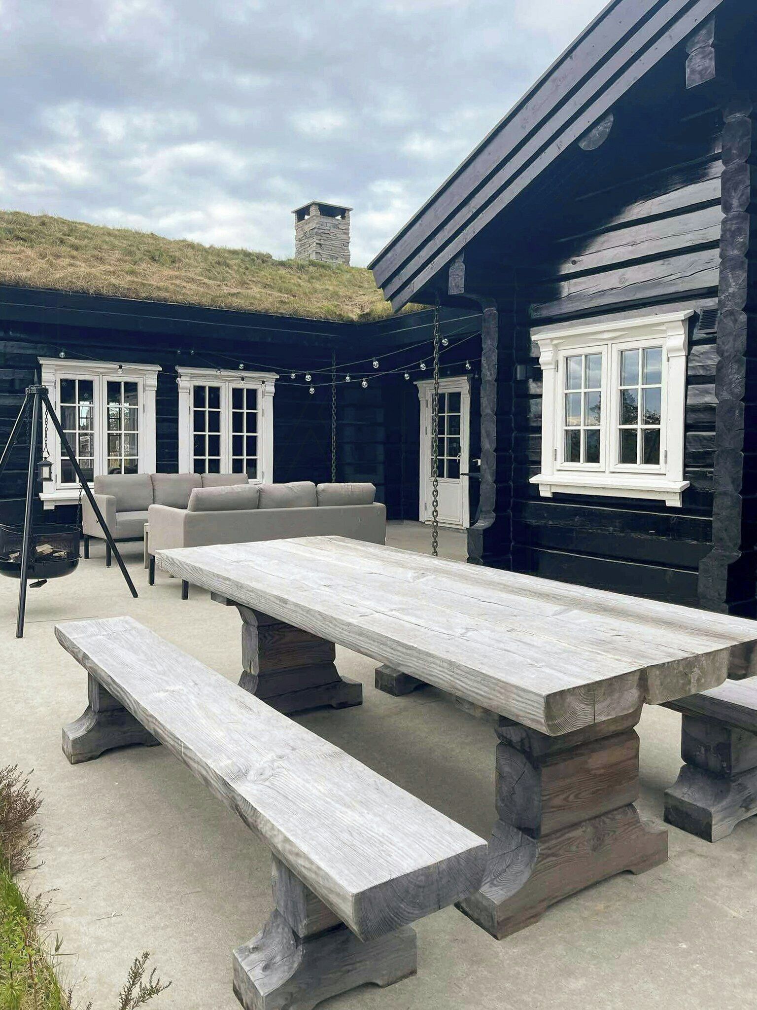 A wooden cabin with a thatched roof, a large dining table, benches, and a sofa.