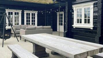 A wooden cabin with a thatched roof, a large dining table, benches, and a sofa.