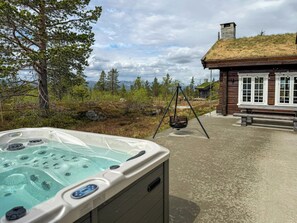 A hot tub with a view of a cabin and forest.