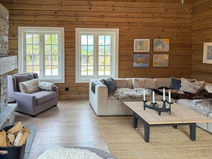 L’intérieur chaleureux d’un chalet avec une cheminée en pierre, deux canapés, une table basse et des œuvres d’art accrochées aux murs.